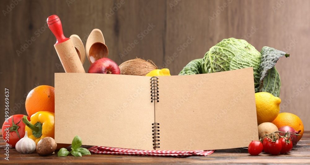 Fototapeta premium Open recipe book, kitchen utensils and fresh products on wooden table, closeup. Space for text