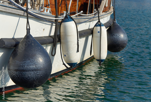 Foto Black and white fenders hanging from the side of a boat, floating on calm water