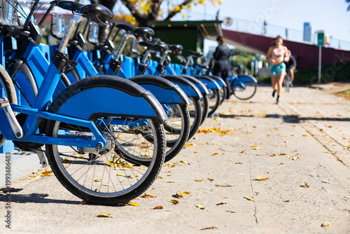 Public city bike sharing station in autumn. Modern automated bicycle rental service with yellow fallen leaves on the ground. Urban eco-friendly transport concept during fall season.