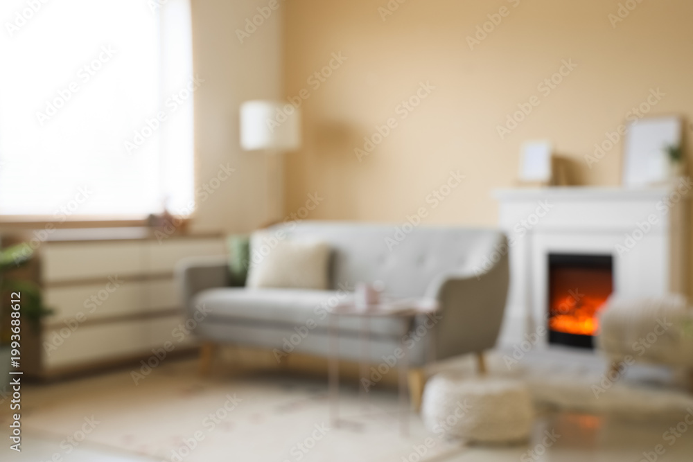 Fototapeta premium Blurred view of living room with grey sofa, commode and fireplace
