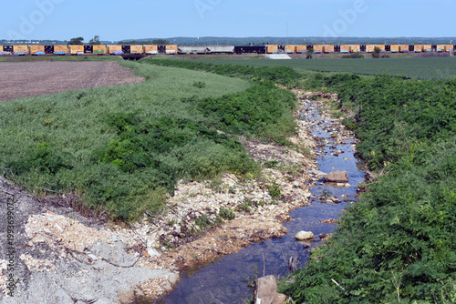 A stream running towards a train going over a bridge.