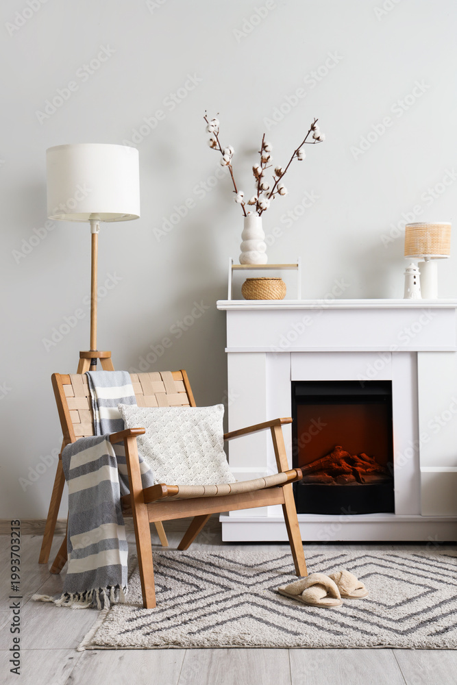 Fototapeta premium Fireplace, wicker armchair and vase with cotton flowers near white wall in interior of living room