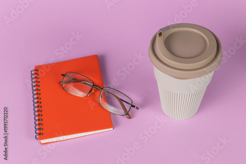 Vibrant Workspace: Orange Notebook, Eyeglasses, and Coffee Cup on Pink Background