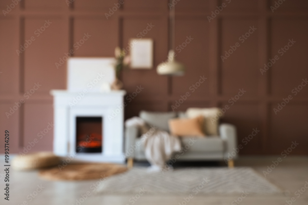 Fototapeta premium Blurred view of cozy living room with grey sofa, wicker pouf and stylish fireplace