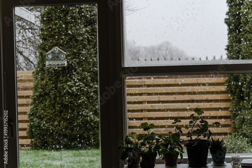 Window with view to garden and falling snow in home interior.