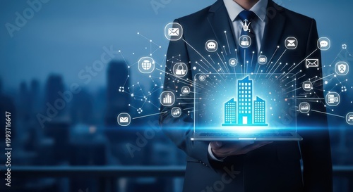 Businessman holding a laptop with a glowing digital building hologram and network icons, representing smart city technology, real estate management, and global business connectivity