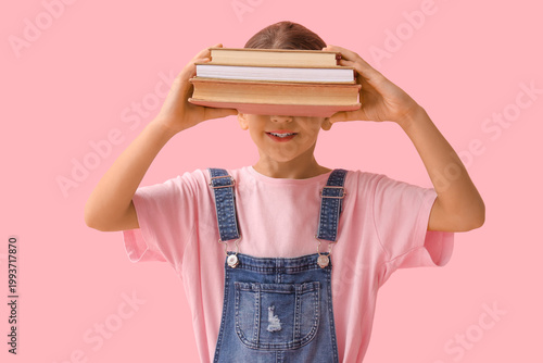 Little girl hiding face behind books on pink background