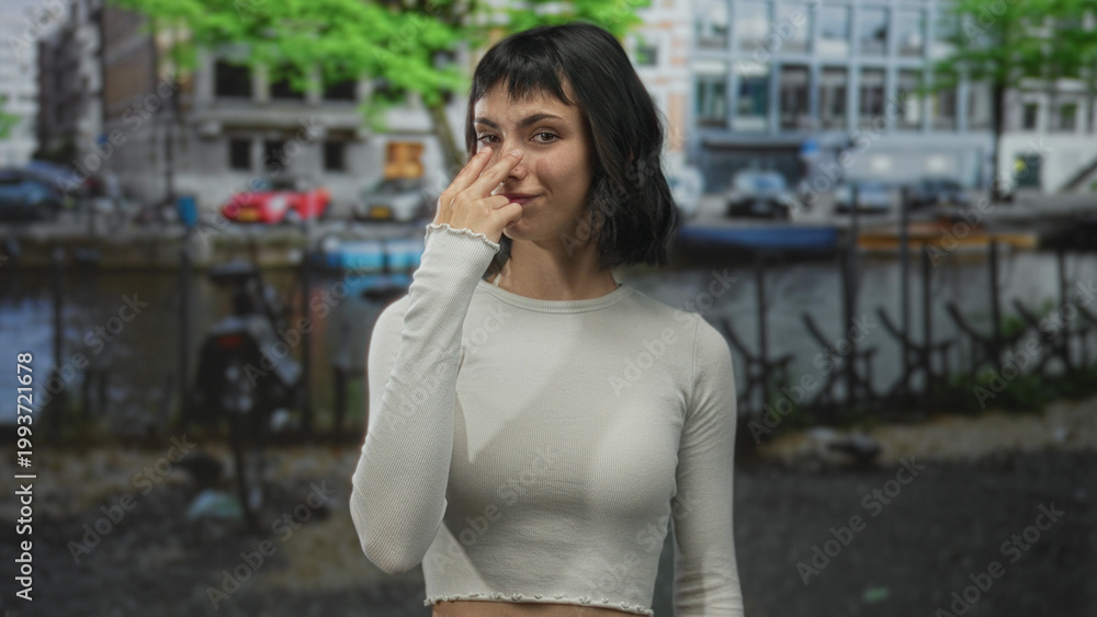 Fototapeta premium Young hispanic woman pointing finger at camera on street in amsterdam with direct gaze; vigilance alertness.
