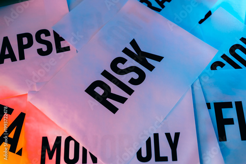 Words like risk, monopoly, and collapse are printed on sheets of paper, arranged in an overlapping fashion. The setting features a mix of colors that draw attention to the messages displayed