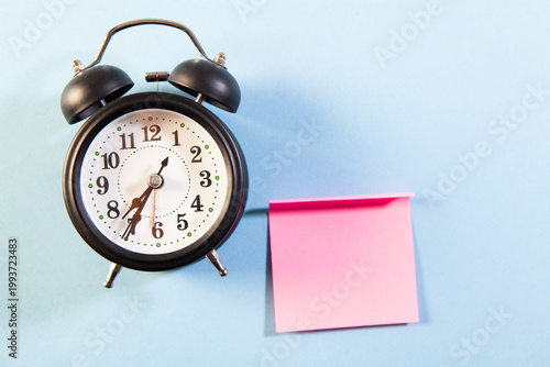 Alarm clock and sticky note on blue background. Time management concept
