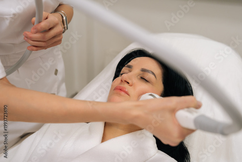 Quadro su tela Close-up of relaxed woman with closed eyes receiving microneedle radiofrequency face lifting procedure from dermatologist for skin tightening and rejuvenation in professional aesthetic clinic