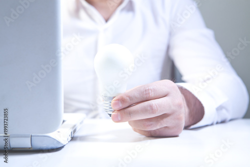 Businessman holding a light bulb in front of a laptop computer.