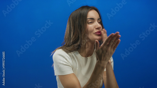 Fényképezés Cheerful young hispanic woman blowing kiss with hand raised to lips in blue studio setting; affection love romance