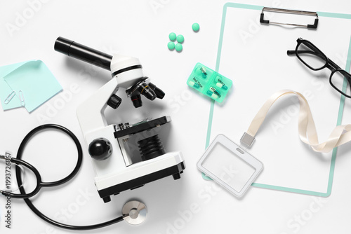 Modern microscope with stethoscope, clipboard and medicine on white background