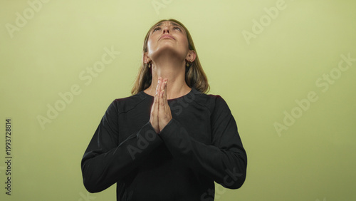 Photography Young blonde woman pressing hands together in prayer, looking upward in green studio; hope faith patience