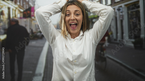 Fotografie Woman holding hands on head and grimacing in a busy city street while pedestrians pass and storefronts line the sidewalk; stress frustration