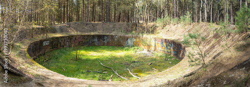Striking ammunition destruction pit in the forest (Lommel - Belgium) with colorful graffiti and green moss in bright sunlight.