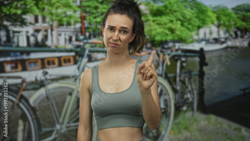 Canvas-taulu Woman pointing finger on street by canal with bicycle parked against canal railing and building facades visible; doubt