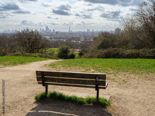 Empty park bench with city skyline view at the top of Parliament Hill on Hampstead Heath, London, UK