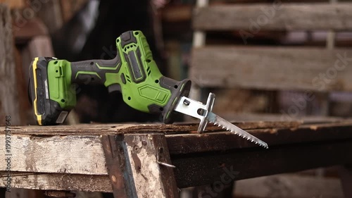 Cordless reciprocating saw on a wooden work surface. The tool lies on an old wooden structure in the workshop. Cordless reciprocating saw for professional and household work. Compact electric saw