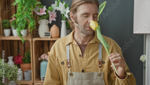 Bild auf Leinwand Man florist in studio smelling yellow tulip, holding stem to nose and closing eyes while arranging flowers; serenity