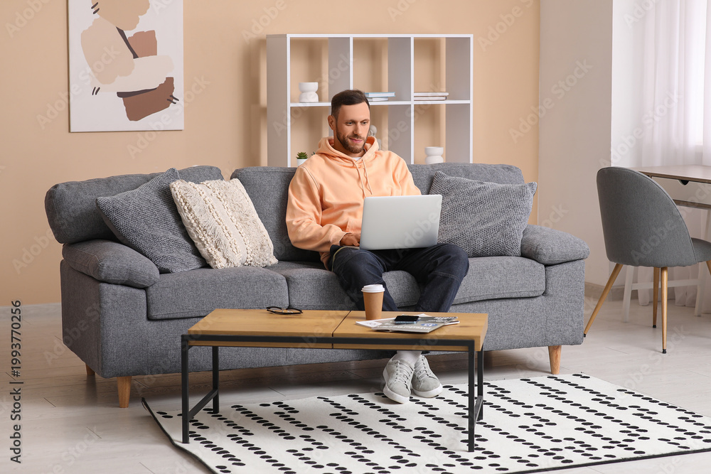 Obraz premium Handsome man using laptop on sofa in living room