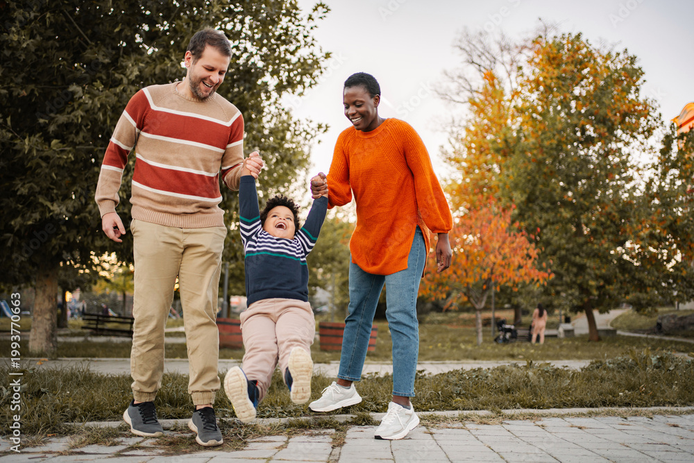 Fototapeta premium Happy family holding child's hands and swinging in autumn park