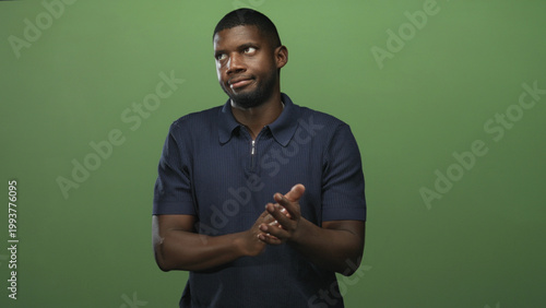 Man clapping hands with an eye roll and sardonic expression, navy polo visible in green studio setting; dry sarcasm.