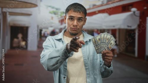 Fotografija Man holding a fan of us dollars and pointing finger toward camera on crowded shopping street; confidence persuasion