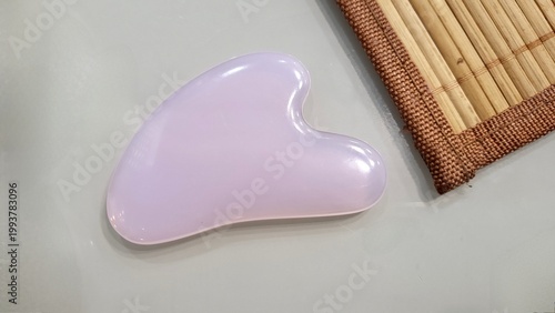 A pink Guash scraper and a heart-shaped facial massager are lying on the table.