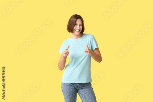 Young woman in blank t-shirt pointing at viewer on yellow background