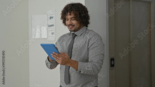 Tableau sur toile Man tapping blue tablet with hands in building, wearing shirt and tie while smiling at screen; confidence productivity