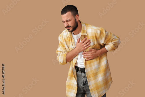 Young man suffering from heart attack on beige background