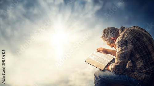 Man in prayer reading scripture under a radiant sky in peaceful reflection