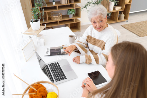 Happy senior woman and her granddaughter with gadgets sitting at home