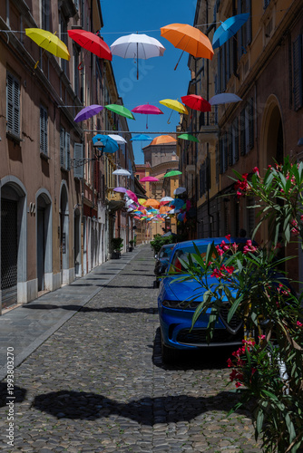 City street in Modena, Italy with rainbow colored umbrellas overhead, vibrant urban scene, summer atmosphere, travel destination