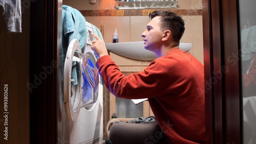 Εκτύπωση καμβά Young man wearing a red sweatshirt completing household chores, loading a front