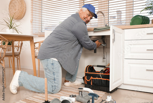 Mature male plumber repairing sink in kitchen