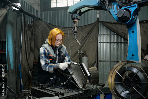 Woman operator removes welded part from robotic welding cell