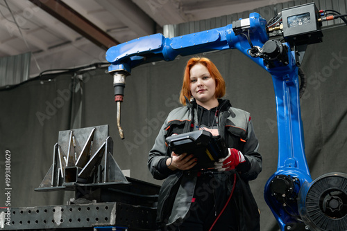 Female technician operates automated welding robot in workshop