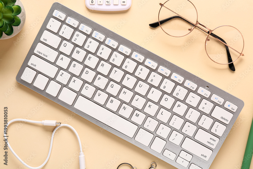 Fototapeta premium Modern office workspace flat lay with wireless keyboard, eyeglasses, cable, calculator and succulent plant on pastel yellow desk, top view minimalist remote work technology background