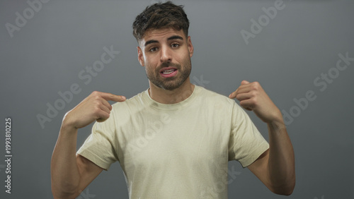 Schilderij op canvas Man wearing casual beige short sleeve t shirt points both index fingers to chest in gray studio; confidence