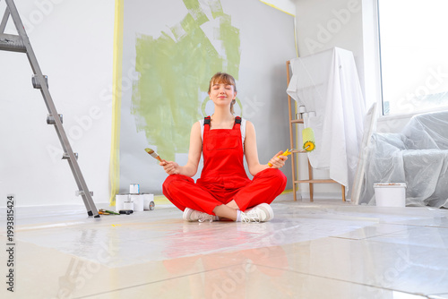 Female decorator with paint roller and brush meditating during repair in room