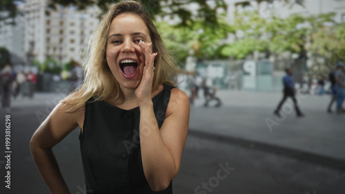 Obraz na plátně Woman shouting with hands cupped to mouth on urban street with buildings and trees visible; joy celebration public expression