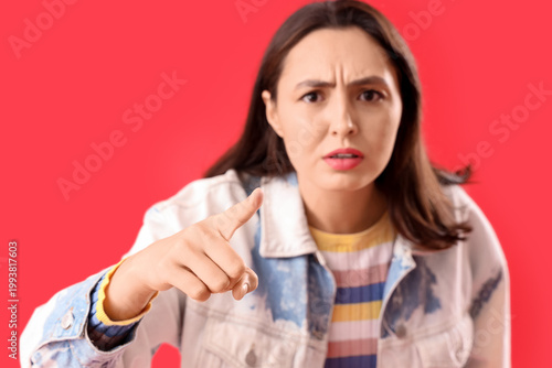 Fotografie Young woman pointing at viewer on red background, closeup