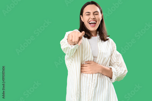 Obraz na płótnie Laughing young woman pointing at viewer on green background