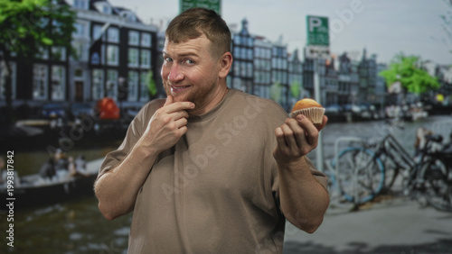 Photos Man holding cupcake, hand to mouth on street by canal and bicycles in amsterdam; hesitation temptation