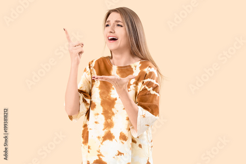 Bilde på lerret Young woman pointing at something on beige background