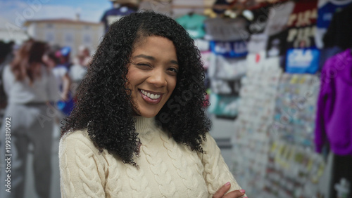 Canvastavla African american woman smiling at camera by a colorful souvenir stall in street market; happiness warmth
