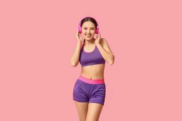 Young woman in sportswear listening to music on pink background